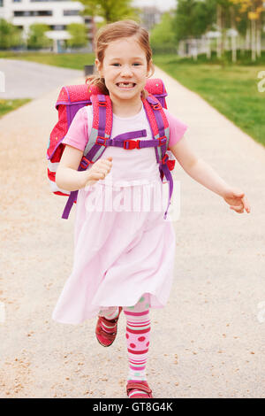 Schulmädchen mit rosa und lila Schultasche lächelnd und laufen in Richtung Kamera zeigt ihre Zahnlücken, Deutschland Stockfoto