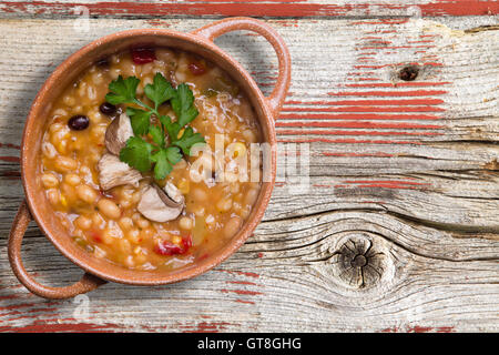 Bohnen und Gerste Suppe mit frischen in Scheiben geschnittenen Champignons und ein Bund Petersilie garniert serviert in einer Schüssel auf einem rustikalen Holztisch mit Stockfoto