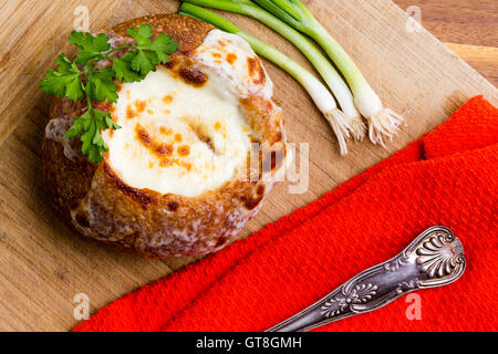 Leckere heiße cremige Zwiebelsuppe serviert in einer Brotschale garniert mit frischer Petersilie mit einem bunten roten Serviette und frischen spri Stockfoto
