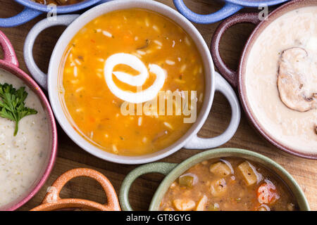 Draufsicht der sortierten Suppe in Schalen mit Griffen mit Fokus auf eine Tasse Hühnerbrühe mit wildem Reis garniert mit einem Strudel Stockfoto