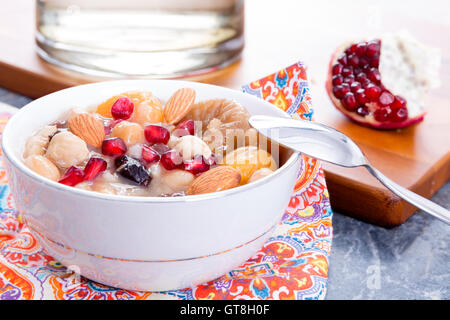 Türkische Noahs Pudding oder Ashure mit Granatapfel und Nüssen in einer weißen Schüssel auf einer bunten Serviette zum Nachtisch serviert Stockfoto