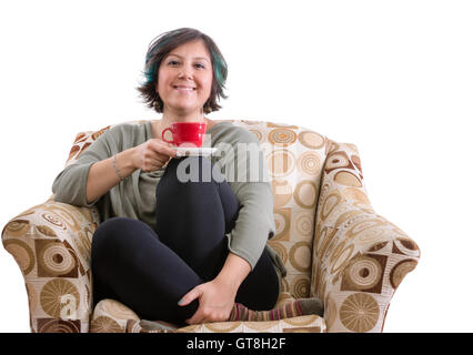 Einzelne Erwachsene Frau mit Lächeln sitzen mit roten Becher und gekreuzten Beinen in Sofa Sessel auf weißem Hintergrund Stockfoto