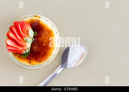 Köstliche Pudding Dessert gekrönt mit Erdbeerscheiben aus Sichtwinkel mit Löffel über Braun Tischdecke Stockfoto