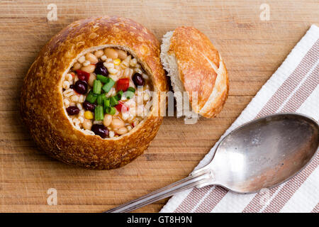 Draufsicht der köstlichen Brotschale mit Bohnen, Gerste, Mais und Gemüse neben Deckel und Löffel auf Tisch Stockfoto