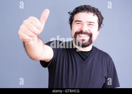 Im mittleren Alter bärtiger Mann im schwarzen Hemd klebt seine Hand nach außen mit Daumen und glückliches Lächeln über grauen Hintergrund Stockfoto