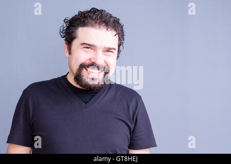 Taille bis Porträt von reifer Mann mit Bart und dunklen Locken tragen Schwarzes T-Shirt und lachen oder Lächeln in die Kamera im Studio Stockfoto