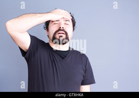 Taille bis frustriert bedauernd Mann mit Bart tragen dunkle T-Shirt halten Kopf und Hand auf Stirn im Studio mit grauen Backg Stockfoto