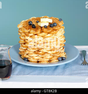 Stapel von Waffeln auf blaue Platte mit Butter und Blaubeeren und Ahornsirup in Krug auf der Seite Stockfoto