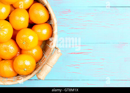 Top-down-First-Person Perspektive Stroh Korb gefüllt mit Clementine Orangen über gemalte blaue Holztisch und Kopie sp Stockfoto
