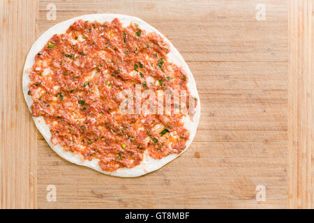 Einzigen traditionellen türkischen Lahmacun mit Bohnenkraut Hackfleisch / Faschiertes und Gemüse auf einem Teig bereit, auf einem hölzernen hacken Bo Kochen Stockfoto