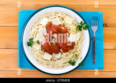 Top-down Ansicht auf Teller Spaghetti Pasta garniert mit Grana Padano Käse Bits, italienische Petersilie und roten Soße über blauen Platz Stockfoto