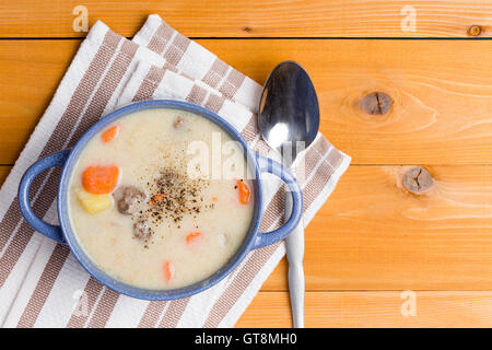 Köstliche Suppe Vorspeise mit Frikadellen und gesundes frisches Gemüse mit gemahlenem Pfeffer bestreut und serviert in einer blauen Tasse auf einem Stockfoto