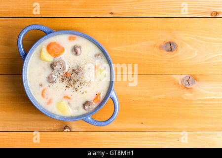 Nahrhafte Fleischklößchen Suppe mit Gemüse garniert mit gemahlener schwarzer Pfeffer und serviert in einer blauen Schüssel auf einem natürlichen Holz Tisch wi Stockfoto