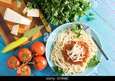 Blick von oben auf Runde Teller mit frisch zubereiteten Spaghetti mit roter Soße, Petersilie und Greyerzer Käse neben Messer gekrönt Stockfoto