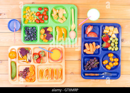 Top-down Ansicht von bunten Kunststoff Lunch Schalen gefüllt mit leckeren Stücke von Obst und Gemüse entlang Seite Tassen Milch oder ju Stockfoto