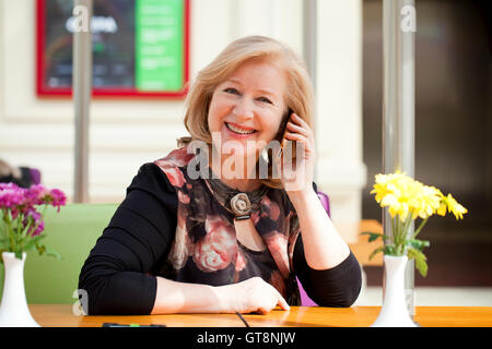 Reife schöne blonde Frau ruft auf einem Handy beim Sitzen in einem Café Stockfoto