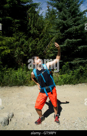 GenY männlich nimmt Selfie Foto in Natur iPhone6 Smartphone Technologie Onroute über Schotterweg nach Brandywine Wiesen Whistler, BC Stockfoto