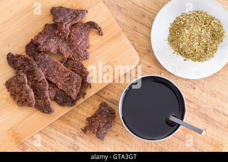 Herstellung von traditionellen hausgemachten Dörrfleisch oder Biltong mit dünnen Streifen aus magerem Rind-Fleisch auf ein Schneidebrett mit Teriyaki-sauce Stockfoto