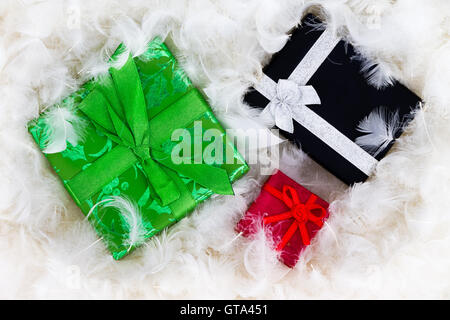 Dekorative Weihnachtsgeschenke eingebettet in üppige weiße flauschige Federn in einem Konzept des leichten Gewichts von oben gesehen Stockfoto