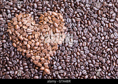 Hintergrund aus Draufsicht auf Haufen von Kaffeebohnen Einschub unter dunkleren verteilt auf einer Fläche in Herzform gefertigt Stockfoto