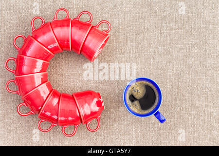 Elf rote Becher gestapelt in der Form des Buchstabens C neben einer blauen Tasse voll Kaffee Konzept über das erste, was in der morni Stockfoto