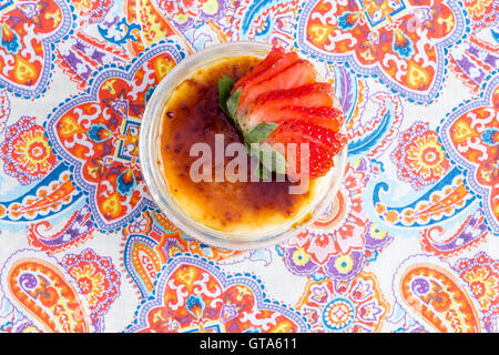 Leckeren Schüssel mit Crème brûlée mit frischen Erdbeeren auf paisley Tisch platziert, wie aus einer Draufsicht zu sehen Stockfoto