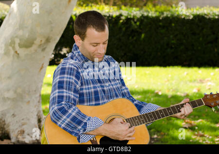 Erstellen Musik - Mann spielt akustische Gitarre im Park. Stockfoto