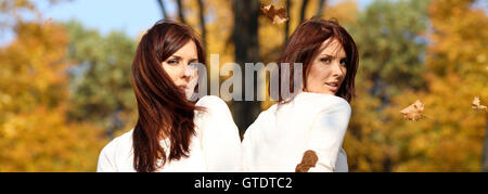 Lächelnde junge attraktive Frauen mit Herbst Ahorn Blätter im Park im Herbst im freien Stockfoto