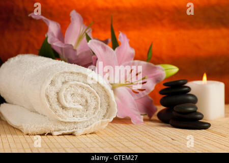 Spa-Konzept der Lilie Blume, Handtücher, Meersalz, Kerze und Crystal Rock rosa Quarz auf warmen hölzernen Hintergrund. Stockfoto