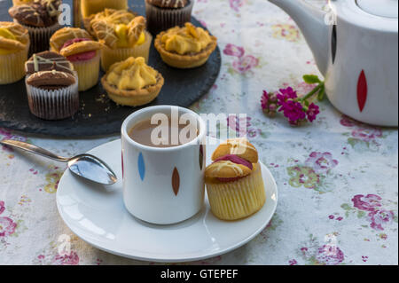 Tee mit Kuchen und Makronen auf dem Tisch im Garten einrichten Stockfoto