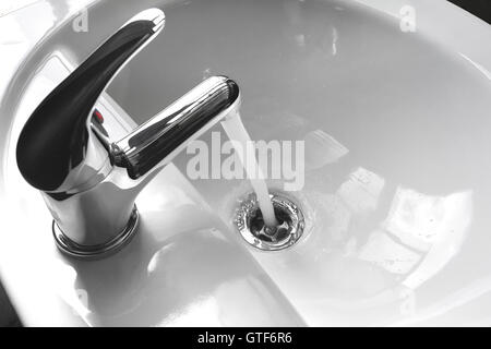 Wasserhahn Wasserhahn mit fließendem Wasser in einem weißen Waschbecken. Stockfoto