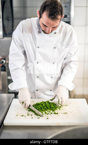 Chef hacken Petersilie Blätter mit einem Messer auf ein Schneidebrett Stockfoto