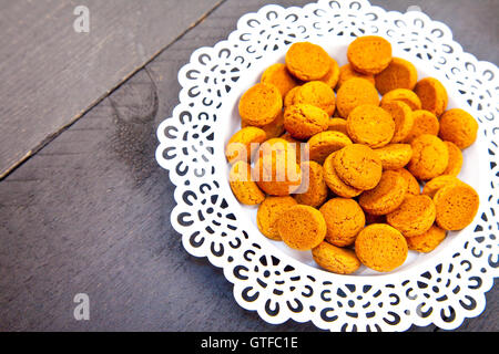 Traditionellen niederländischen Süßigkeiten Pepernoot auf weißen Teller auf schwarzem Hintergrund aus Holz Stockfoto