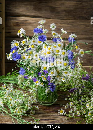 Bouquet von Kamillen und Kornblumen in der Vase auf dem Holztisch. Stockfoto