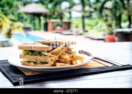 Club Sandwich Snack mit Pommes Frites auf Platte Pool inmitten der tropischen Natur Stockfoto