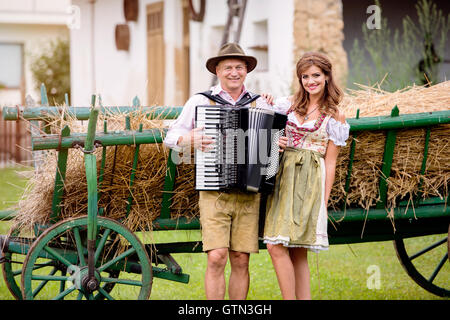 Paar in bayerischer Tracht mit Akkordeon, Heuwagen Stockfoto