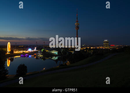 Panorama der Olympiapark München mit einem Sommer fair in der Abenddämmerung mit beleuchteten Olympiaturm, BMW Welt, Allianz Arena Stockfoto