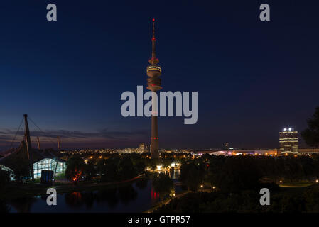 Panorama der Olympiapark München in der Abenddämmerung mit beleuchteten Olympiaturm, BMW Welt, BMW Turm und Olympia Bad hall Stockfoto