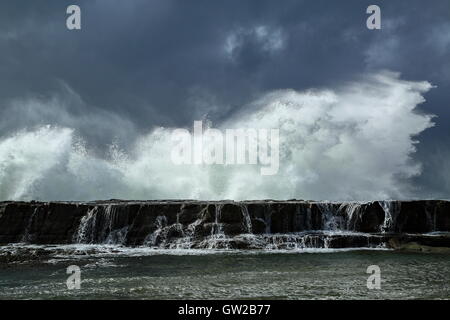 Ein Wintersturm peitscht große und mächtige Wellen, die gegen eine Landzunge, unter einem schweren Himmel abstürzen. Stockfoto