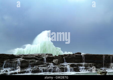 Ein Wintersturm peitscht große und mächtige Wellen, die gegen eine Landzunge, unter einem schweren Himmel abstürzen. Stockfoto