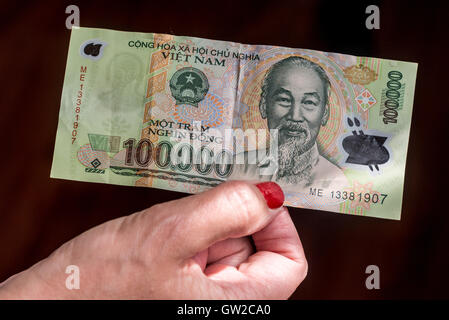 Hand, die vietnamesische Banknote für 100.000 Dong. GBP £3,33 Stockfoto