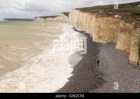 Solitary Man allein stehend auf einem Kiesstrand unterhalb der weißen Klippen von sieben Schwestern mit Blick auf Meer und Wellen. Stockfoto