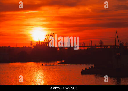 Schwarze Silhouetten von Kränen und Frachtschiffe im Hafen von Varna bei Sonnenuntergang Stockfoto