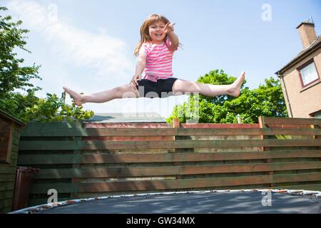 -MODELL VERÖFFENTLICHT. Junges Mädchen auf dem Trampolin. 8 Jahre altes Mädchen springen in der Luft während des Spielens auf einem Trampolin im Garten. Stockfoto