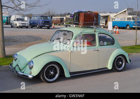 Ein Classic VW Käfer mit Gepäckträger, geparkt mit klassischen VW-Camper im Hintergrund. Stockfoto
