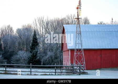 Rote Scheune, Windmühle und Zaun an einem frostigen Morgen in Wisconsin. Stockfoto