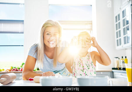 Hübsche Frau und Mädchen spielen mit Essen in der Küche als leichten Blendung durch die Sonne Fenster betritt Stockfoto
