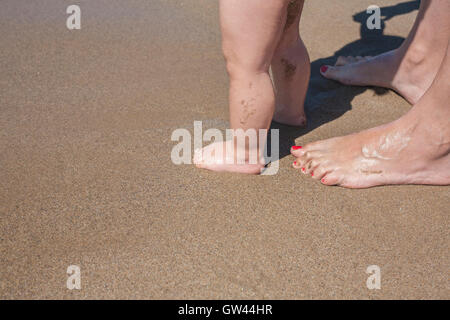 Mutter und Baby Füße am Sandstrand zu Fuß zum ersten Mal Stockfoto