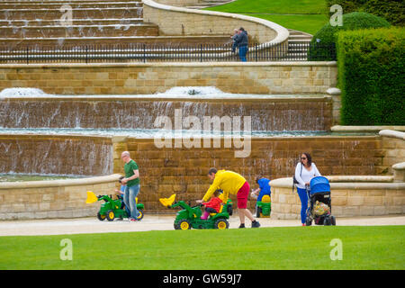 Eltern ihre Kinder mit kleinen Fahrt auf Traktoren auf der Kaskade in Alnwick Castle Garden amüsant Stockfoto