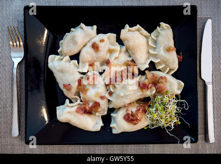 Polnische Pierogi gefüllte Knödel im traditionellen Restaurant auf einem schwarzen Teller serviert und mit Schinken und grünen Sprossen Stockfoto